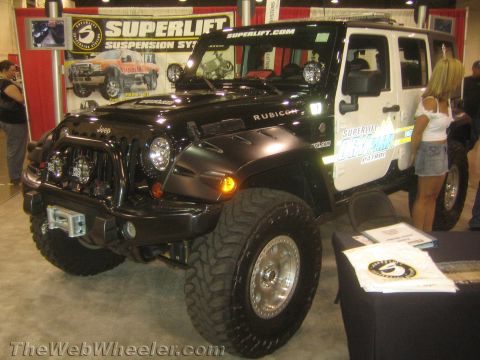 1990 Ford Bronco - black four-door Jeep Wrangler Rubicon with winch bumper sits at a Superlift suspension booth as a woman stands beside it.