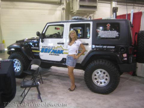 1990 Ford Bronco - woman in a white top and denim shorts poses beside a lifted black-and-white four-door Jeep Wrangler lettered ORV Park Patrol at an indoor s…