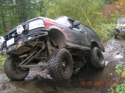 1996 Ford Bronco - A modified black Ford Bronco tackles a challenging off-road course with another vehicle visible in the background.