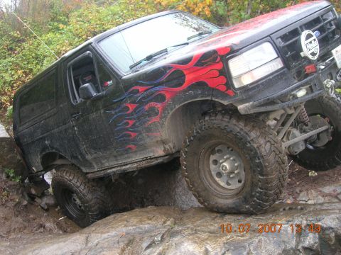 1996 Ford Bronco - 1996 Ford Bronco tackling a difficult off-road trail with large rocks and mud.