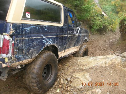 1996 Ford Bronco - A heavily used Ford Bronco tackles a challenging off-road path with significant body damage.