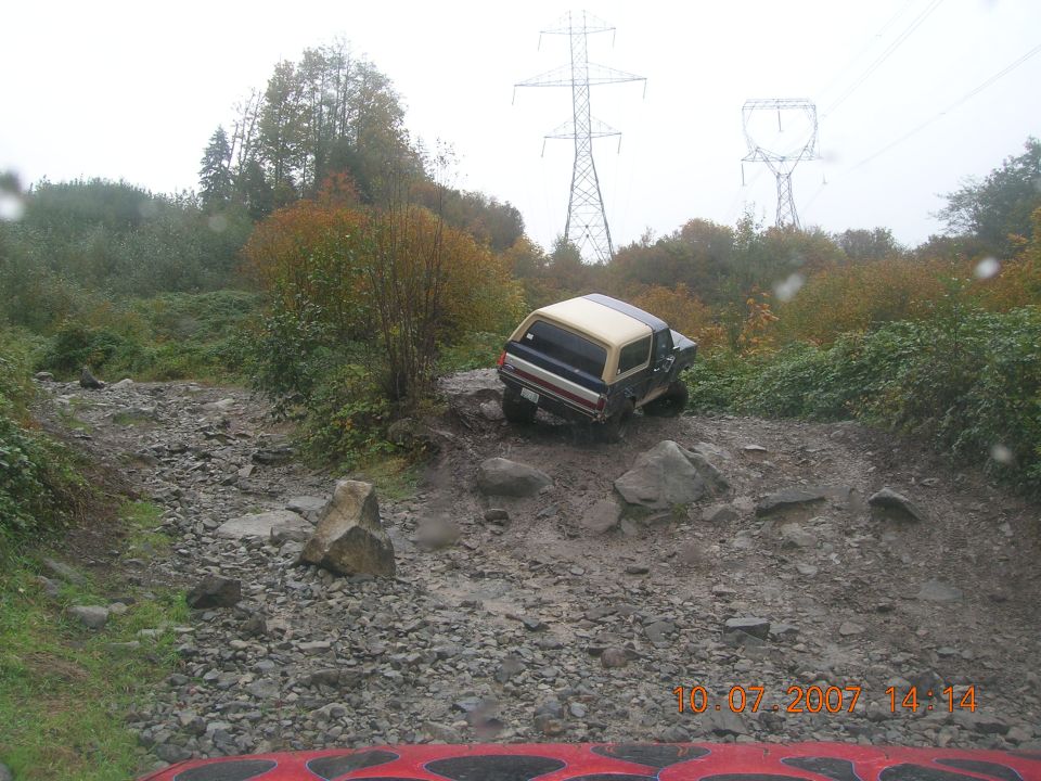 Blue and tan Ford Bronco off-roading on a rocky, muddy trail