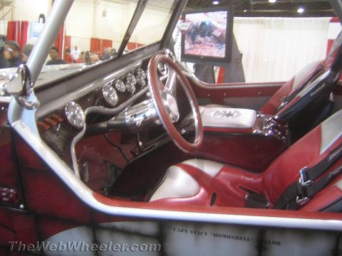 1990 Ford Bronco - custom interior shows a billet steering wheel, gauges and red-and-silver upholstery with a video screen mounted on the roll cage.