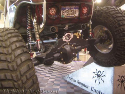1990 Ford Bronco - rear underside of a custom buggy reveals a solid axle, coilover shocks and a Colorado plate reading BMBSHL near a Poison Spyder Customs sig…
