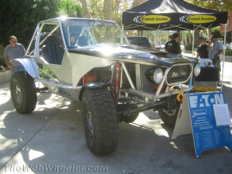 1990 Ford Bronco - silver tube-chassis buggy badged Banshee sits outdoors beside a Detroit Locker canopy and an Eaton spec sign with onlookers nearby.
