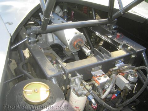 1990 Ford Bronco - close view of a race vehicle's chassis shows a radiator, oil filter, fuel plumbing and tubular roll-cage bars in raw metal.