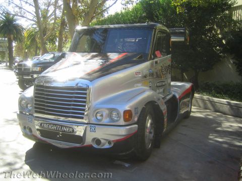 1990 Ford Bronco - silver-wrapped Freightliner racing semi tractor with a chrome grille and number 73 sits parked outdoors among palm trees.
