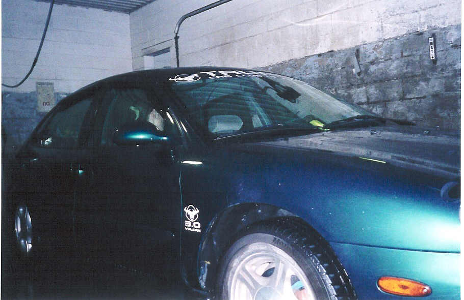 Dark teal Ford Taurus front three-quarter in dim garage with windshield decal