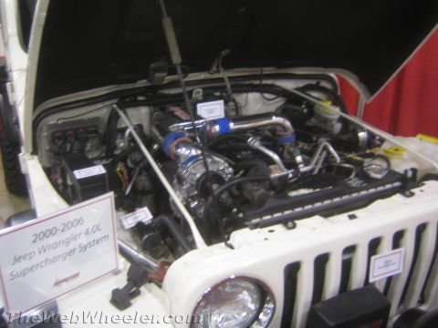 1990 Ford Bronco - engine bay of a white Jeep Wrangler shows a supercharger system beside a sign reading 2000-2006 Jeep Wrangler 4.0L Supercharger System.
