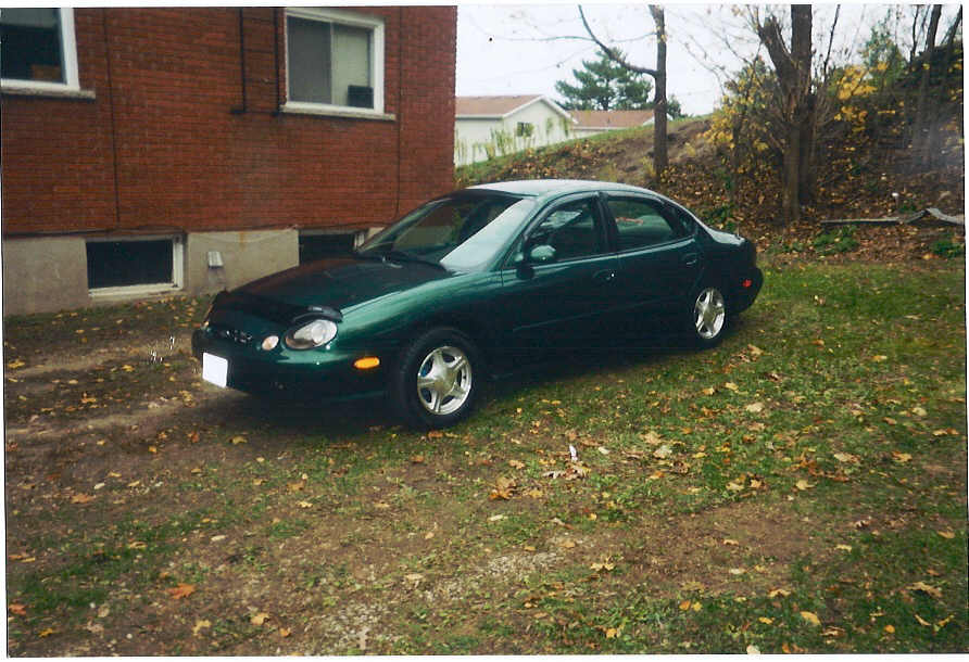 Green sedan parked next to a brick building. Car has a bug deflector on the hood