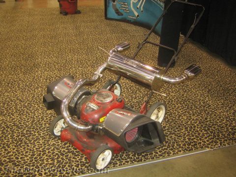 1990 Ford Bronco - red push lawn mower customized with a polished exhaust system and cone air intake on leopard-print carpet.