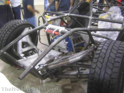1990 Ford Bronco - bare tube-frame off-road race chassis fitted with a blue V8 engine and red coilover shock on display.