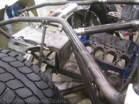 1990 Ford Bronco - close-up of an off-road tube chassis showing a bare blue engine block, fabricated brackets, and rear tire.