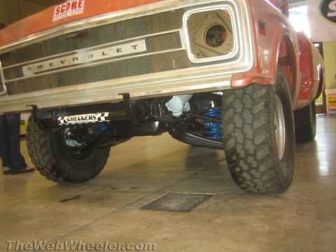 1990 Ford Bronco - Chevrolet-badged front grille and lifted off-road suspension of a red vintage truck with blue coil springs.