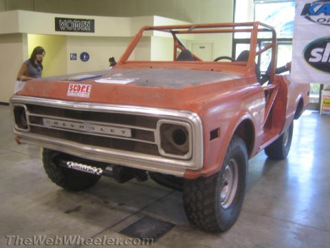 1990 Ford Bronco - vintage orange Chevrolet 4x4 with a roll cage and open top, off-road tires, displayed at an indoor expo.