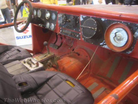 1990 Ford Bronco - spartan cockpit of an old off-road truck shows a worn orange-painted dash, cluster of gauges, floor shifter and black bucket seats; a Suzuk…