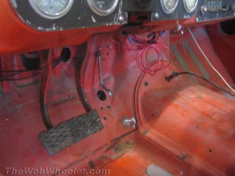1990 Ford Bronco - close view inside an off-road truck shows the bare orange-red metal floor, drilled throttle pedal and loose wiring beneath the gauge panel.