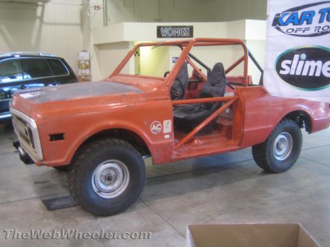 1990 Ford Bronco - orange weathered vintage off-road truck with open top and roll cage on display indoors near a WOMEN restroom sign and Slime banner.