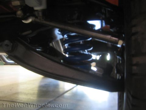 1990 Ford Bronco - dimly lit close-up of a blue coil spring and control arm suspension mounted beneath a vehicle.