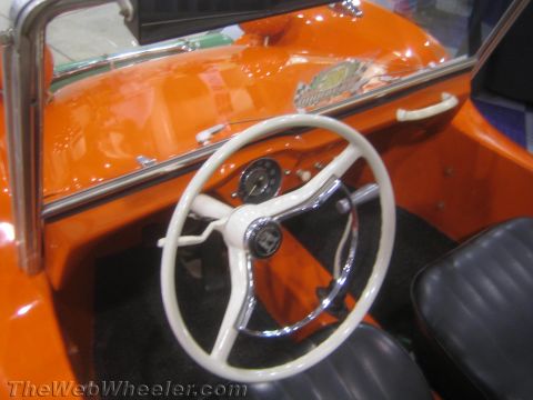 1990 Ford Bronco - simple cockpit of an orange dune buggy shows a white three-spoke steering wheel, a single round gauge and dark carpeting.