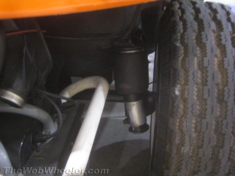 1990 Ford Bronco - close view beneath an orange dune buggy shows a black shock absorber, white tube and a worn rear tire.