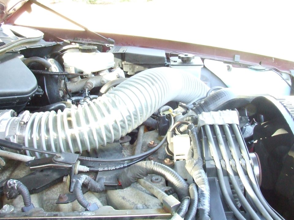 Engine bay of a maroon vehicle showing a large, flexible cold air intake tube connected to the air filter housing
