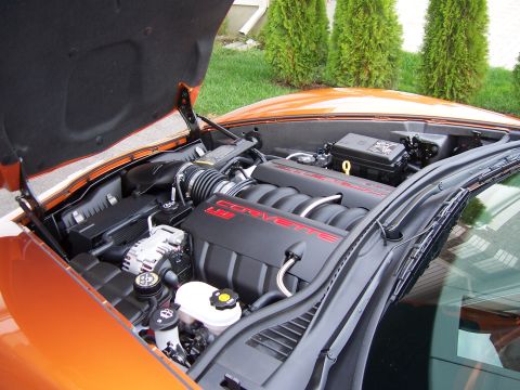 1996 Ford Bronco - The engine bay of an orange Corvette, the LS2 engine, is visible with the hood raised.