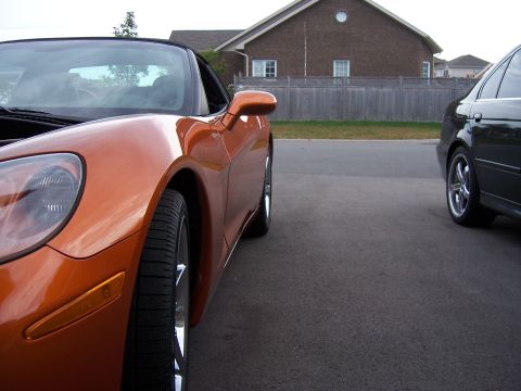 1996 Ford Bronco - An orange convertible sports car is parked on the street next to a dark sedan.