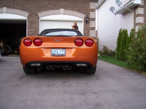 1996 Ford Bronco - The rear of an orange convertible sports car is shown parked in a driveway with a brick garage behind it.
