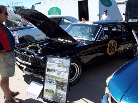 1971 Ford Mustang - A black 1966 Ford Mustang is displayed with its hood open, alongside a display board detailing its history.