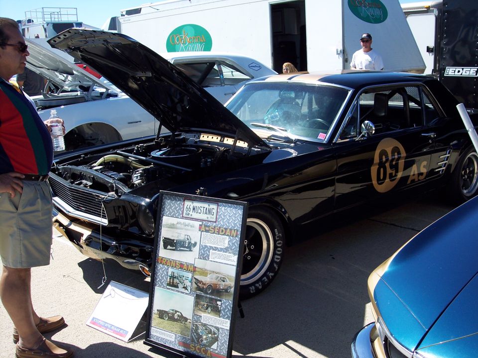 Black 1966 Mustang with gold '89' racing numbers and a display board