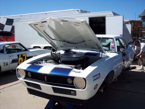 1971 Ford Mustang - Two Chevrolet Camaros at a race track, one with its hood open and being worked on.
