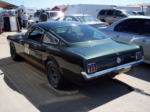 1971 Ford Mustang - A vintage Mustang race car is parked on asphalt, with other vehicles and trailers visible in the background.
