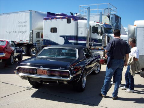 1971 Ford Mustang - A dark blue Mercury Cougar is parked behind a semi-truck, with two men standing nearby.