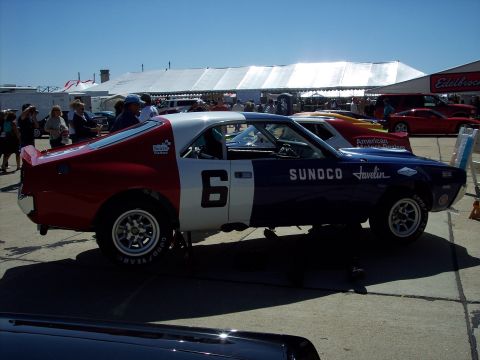 1971 Ford Mustang - A vintage AMC Javelin race car is displayed outdoors with other vehicles and tents in the background.