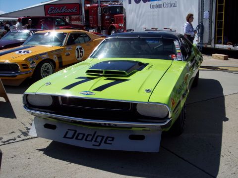 1971 Ford Mustang - A lime green race car with number 77 and Dodge branding is parked next to a yellow race car.