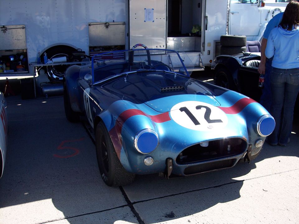Blue race car with red stripes and number 12 on a white circle, parked in front of a trailer