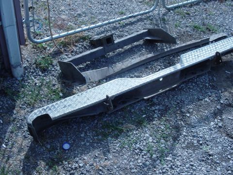 1985 Ford Bronco - Two aftermarket bumpers and a trailer hitch receiver are laid out on a gravel surface.