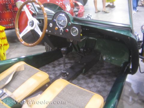 1990 Ford Bronco - cockpit of a green dune buggy features a wood-rimmed steering wheel, round gauges, a tall shifter and tan checkered upholstered seats.