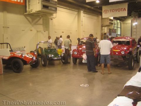 1990 Ford Bronco - Several vintage red and green Meyers Manx-style dune buggies lined up on a concrete floor under a Toyota banner with onlookers.
