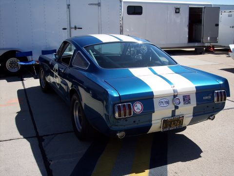 1971 Ford Mustang - A blue and white striped coupe with racing decals is parked on asphalt next to trailers.