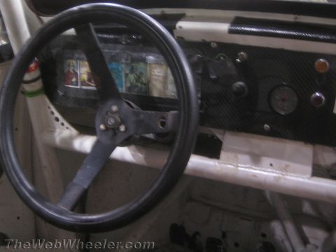 1990 Ford Bronco - Close-up of a black three-spoke steering wheel and a stripped dashboard with a single gauge inside a bare-frame buggy.