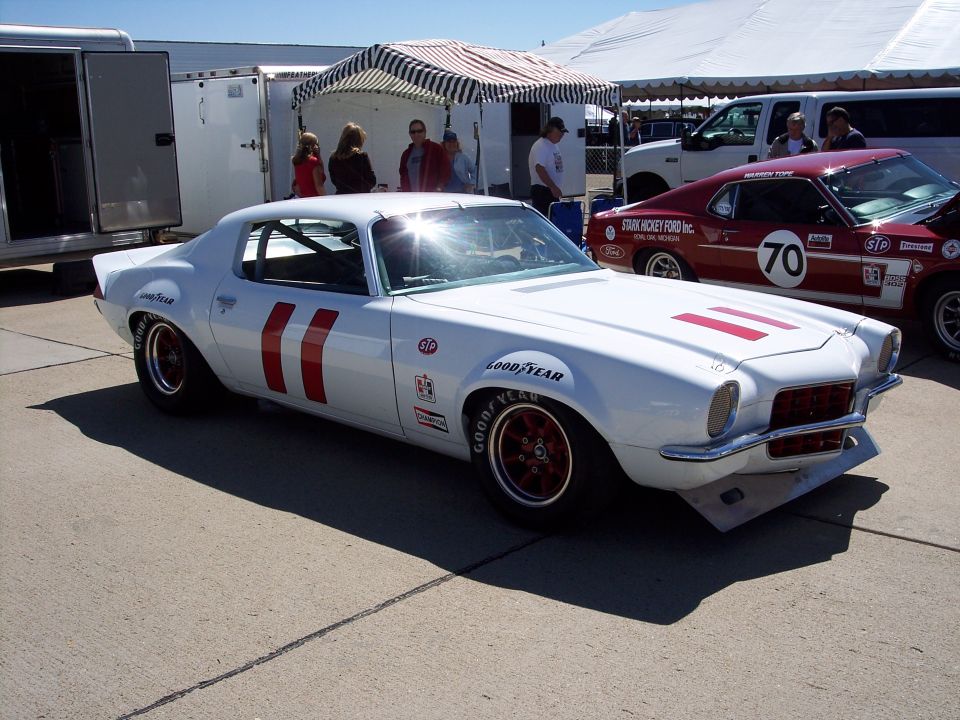 White 1970 Chevrolet Camaro race car with red stripes and Goodyear tires. Another red race car with number 70 is visible behind it