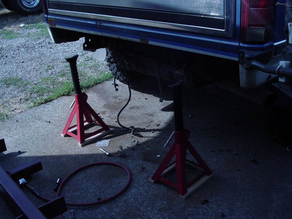 Vehicle frame supported by red jack stands, with a hose on the ground