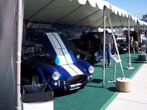 1971 Ford Mustang - A blue Cobra with white racing stripes is displayed under a tent with its hood open, alongside other vehicles.