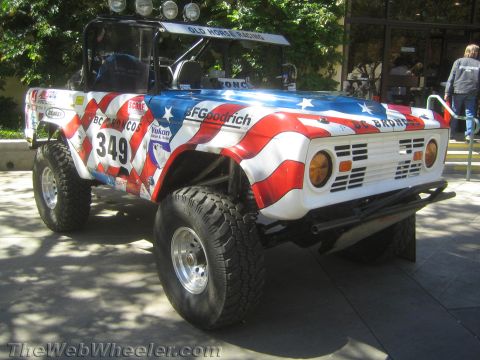 1990 Ford Bronco - early Ford Bronco off-road race truck wrapped in a stars-and-stripes design, numbered 349 and lettered BC Broncos, parked outdoors.