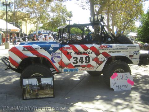 1990 Ford Bronco - Side profile of an American-flag wrapped BC Broncos race truck numbered 349 next to a pink raffle ticket sign at an outdoor event.