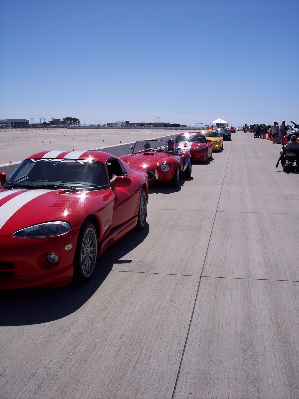 Red Dodge Viper and other sports cars lined up on pavement under a clear blue sky
