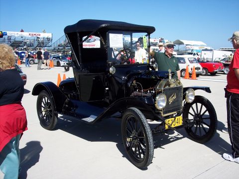 1971 Ford Mustang - A black Ford Model T touring car is displayed outdoors with people and other vehicles in the background.