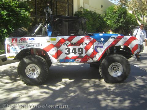 1990 Ford Bronco - Side profile of a red, white and blue BC Broncos off-road race truck numbered 349 with a roof light bar, parked on pavement outdoors.